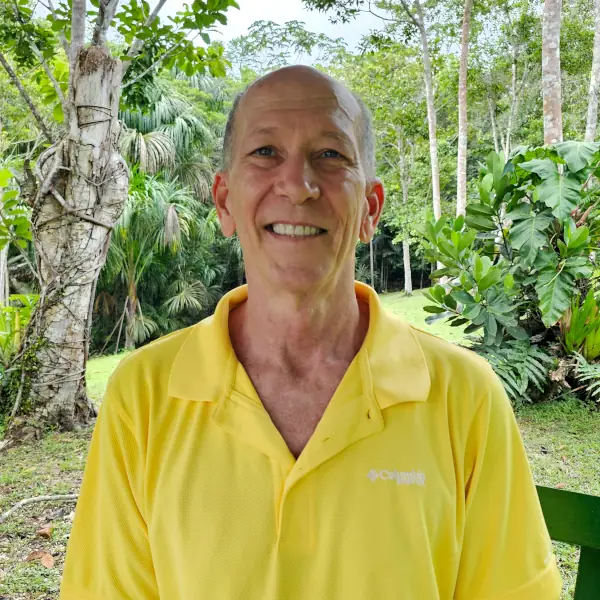 The owner, Jim. Smiling man in a yellow polo shirt with a buzz cut, standing in a lush, green tropical environment.