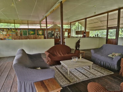 Open-air living room with slip-covered couches, striped rug, and wood floor. Artwork adorns the back wall.
