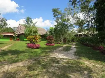 Tropical resort lawn with dirt drive; buildings have thatched roofs, painted vibrant colors.