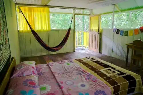 Rustic room with two beds, hammock, and balcony overlooking lush trees